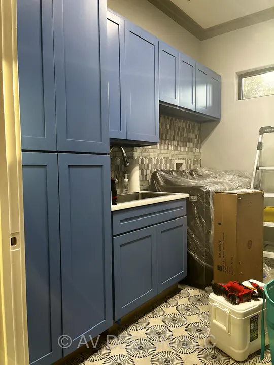 Blue shaker-style laundry room cabinets with a patterned tile floor and tile backsplash