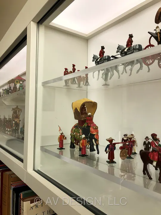 Custom built-in glass display case with lit shelves holding a collection of miniature figures