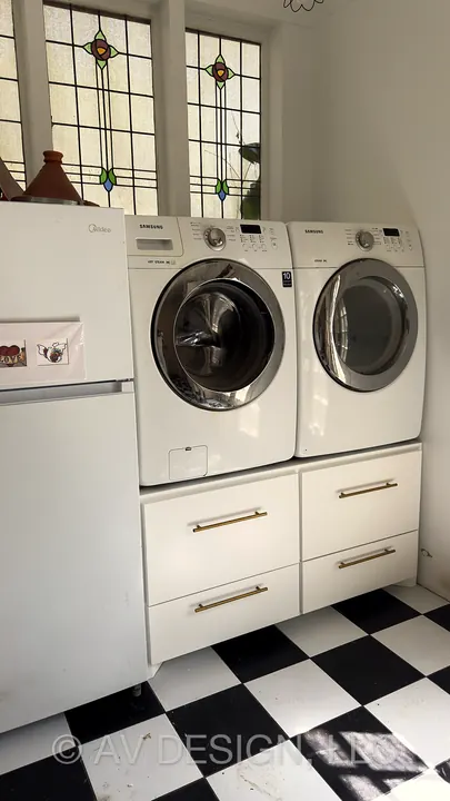 Laundry room with washer and dryer raised on white drawer pedestals with brass pulls