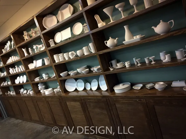 Stained wood open shelving wall displaying white pottery in a paint-your-own studio