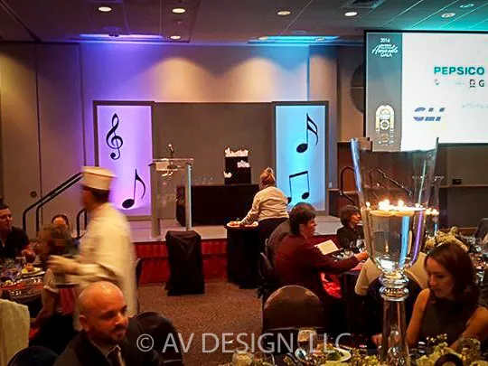 Event stage with backlit panels and music-note cutouts at a corporate dinner