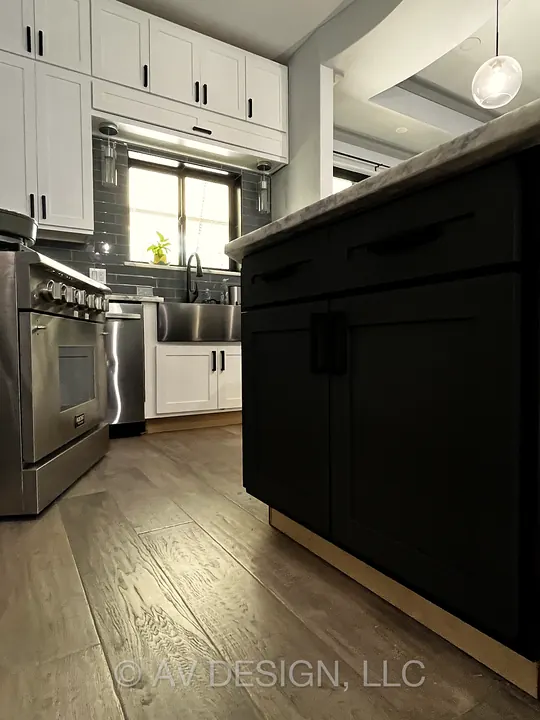 White shaker kitchen cabinets with a black custom island, black pulls and hardwood floors