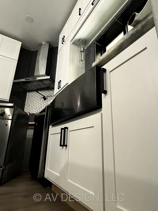 White shaker kitchen cabinets with black hardware beside a stainless range and hood